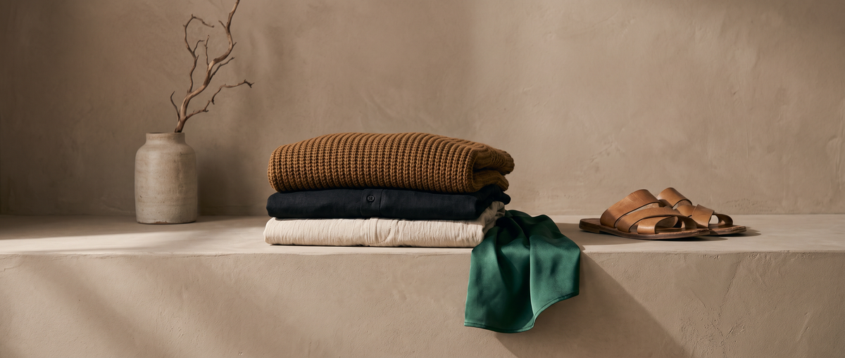 Folded knitwear, shirts and trousers with sandals on a stone ledge
